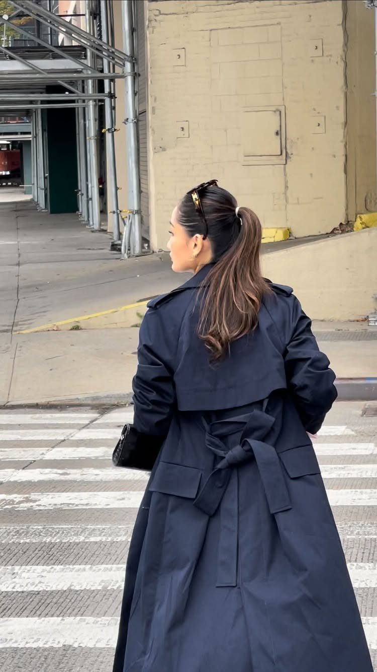 9 Navy Blue Outfit Ideas for Every Setting 6 Woman wearing a long navy blue trench coat walking through a city street.