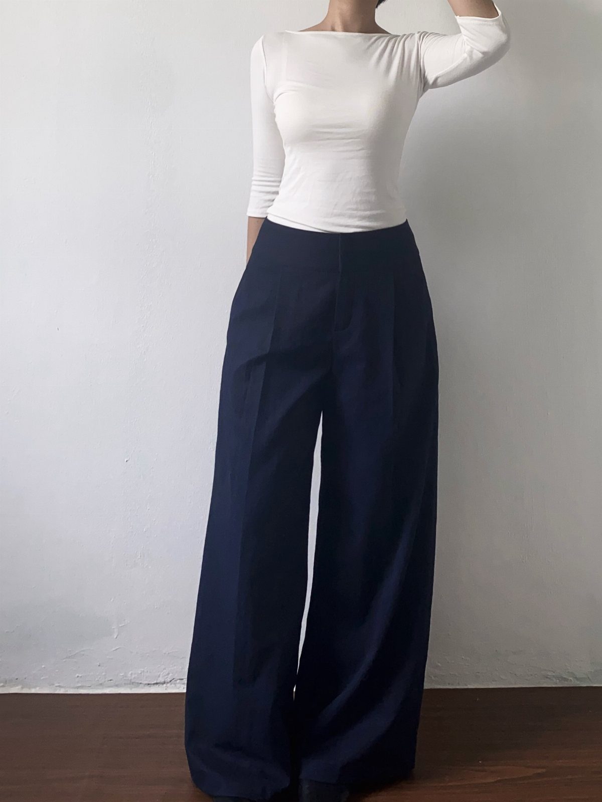 9 Navy Blue Outfit Ideas for Every Setting 1 A person wearing a white long-sleeved shirt and navy blue wide-leg trousers against a white wall.
