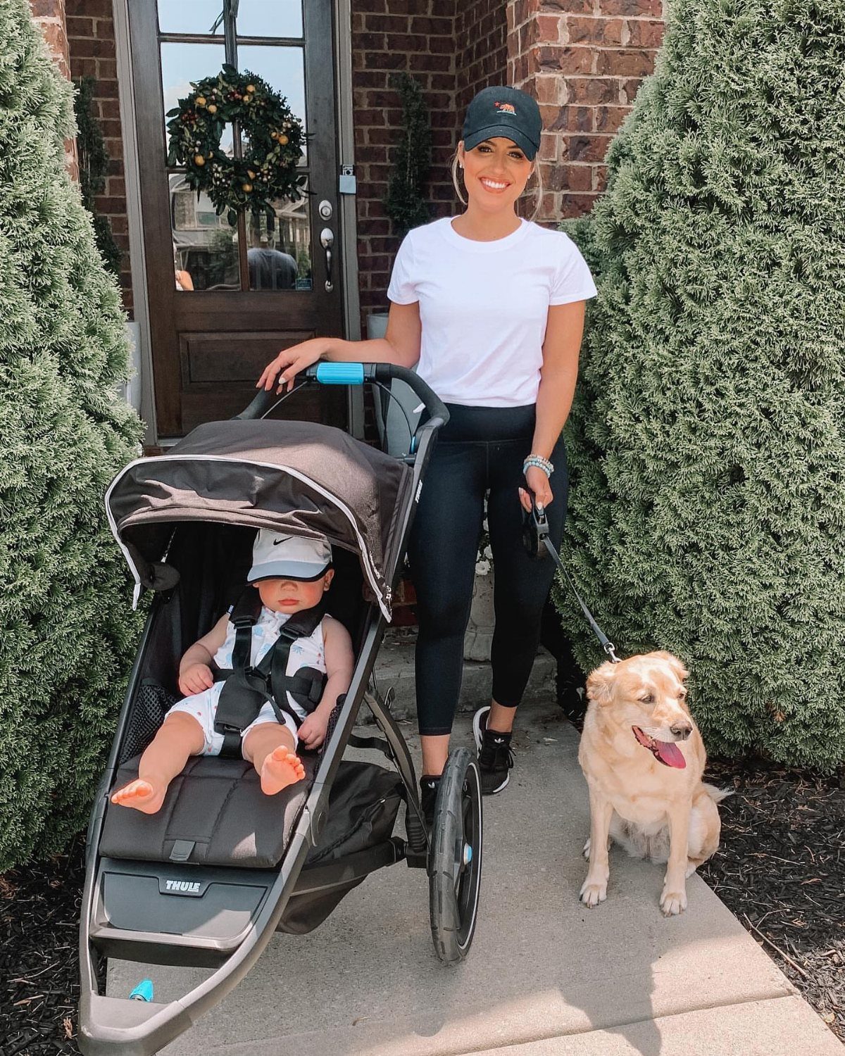 10 Outfit Ideas for Mom: From Classic Days to Mom's Nights Out 6 A woman in athletic wear stands with a baby in a stroller and a dog.