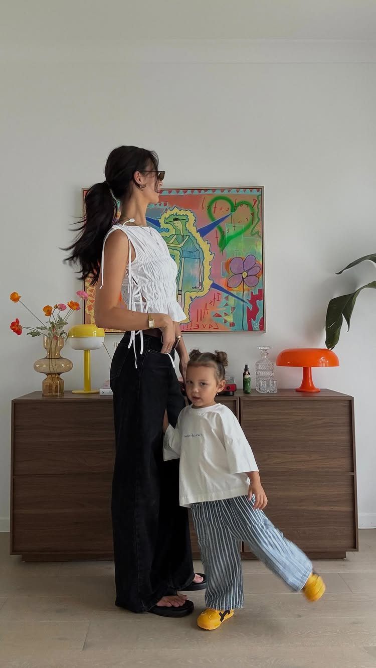 10 Outfit Ideas for Mom: From Classic Days to Mom's Nights Out 5 A woman in a white lace top and black trousers standing with a young child in striped pants.