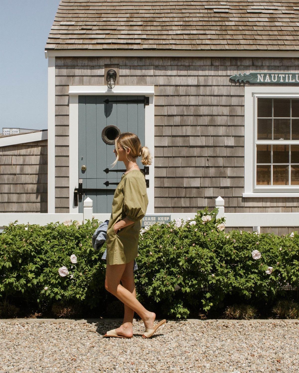 10 Outfit Ideas for Mom: From Classic Days to Mom's Nights Out 9 Blonde woman wearing an olive green dress and tan mules standing outdoors by a shingle house.