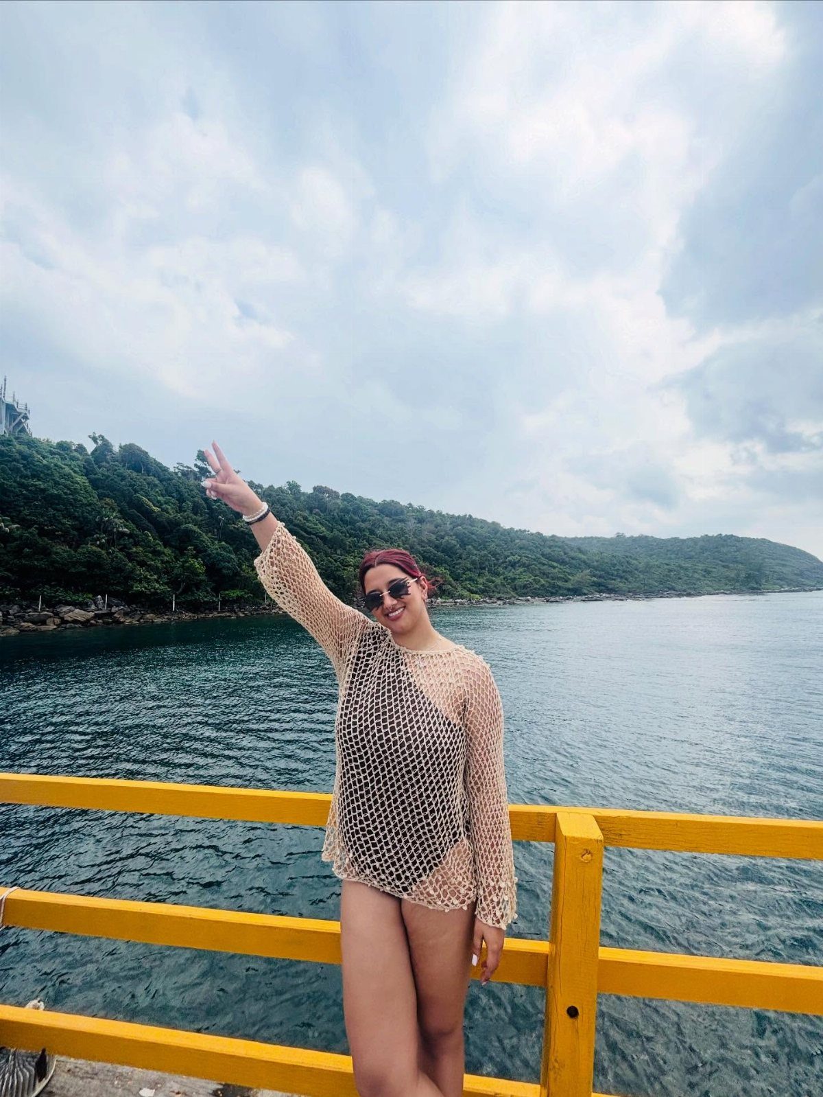 Outfit for Vacation: 13 Ideas for Every Island Moment 2 A woman in a crochet cover-up poses by the ocean next to a yellow railing.