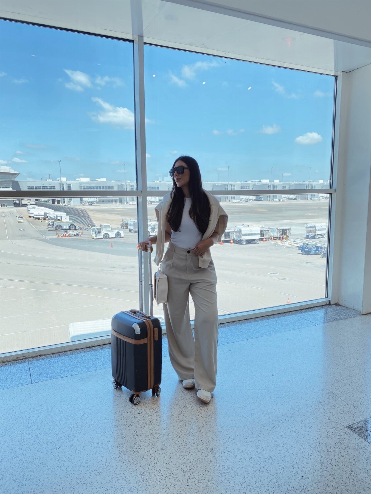 Outfit Ideas for Cancun: 13 Looks for Every Occasion 9 Woman in beige trousers and white top standing with suitcase in airport terminal
