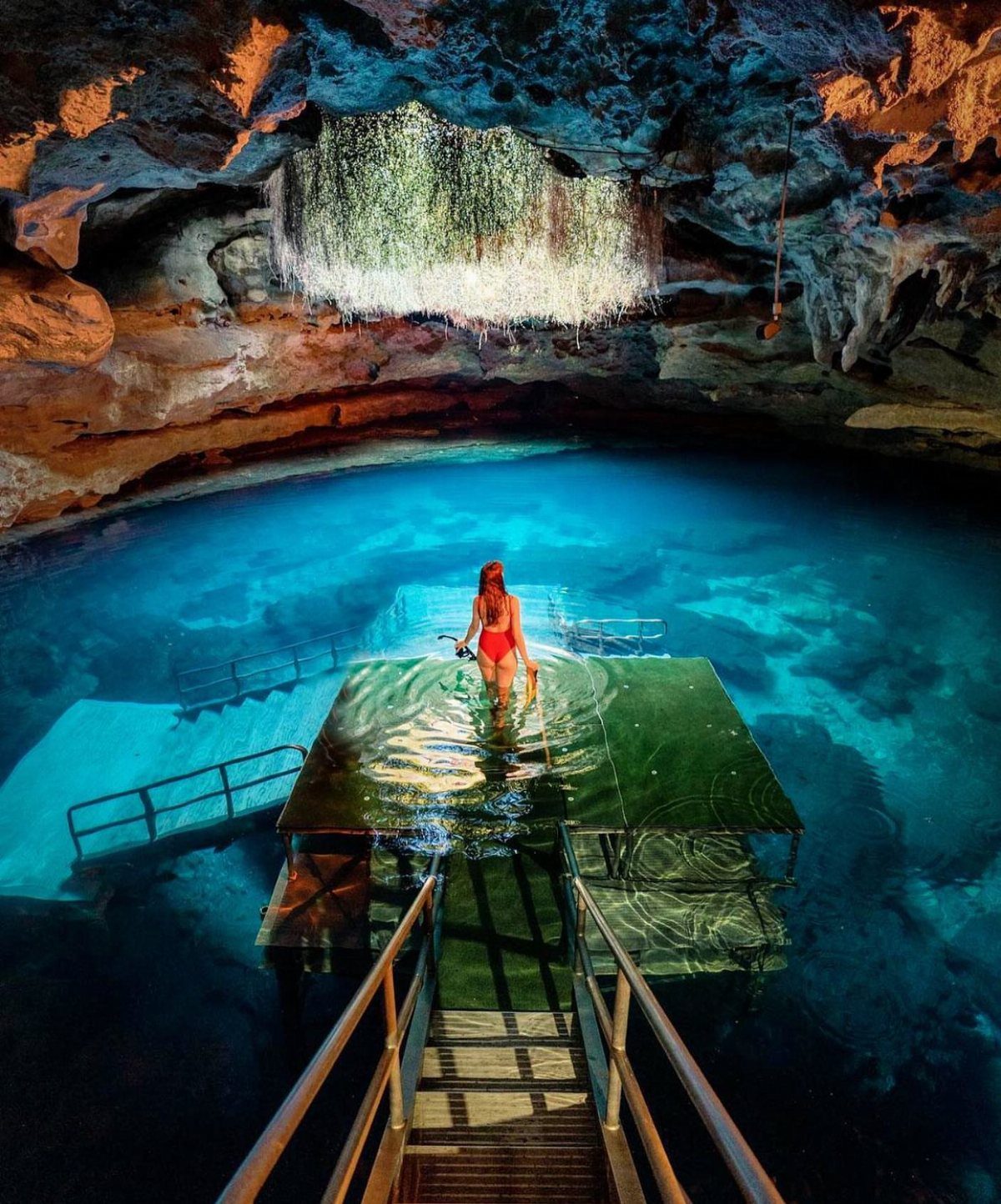 Outfit Ideas for Cancun: 13 Looks for Every Occasion 12 Woman in red swimsuit standing in a blue cenote cave with sunlight streaming in.