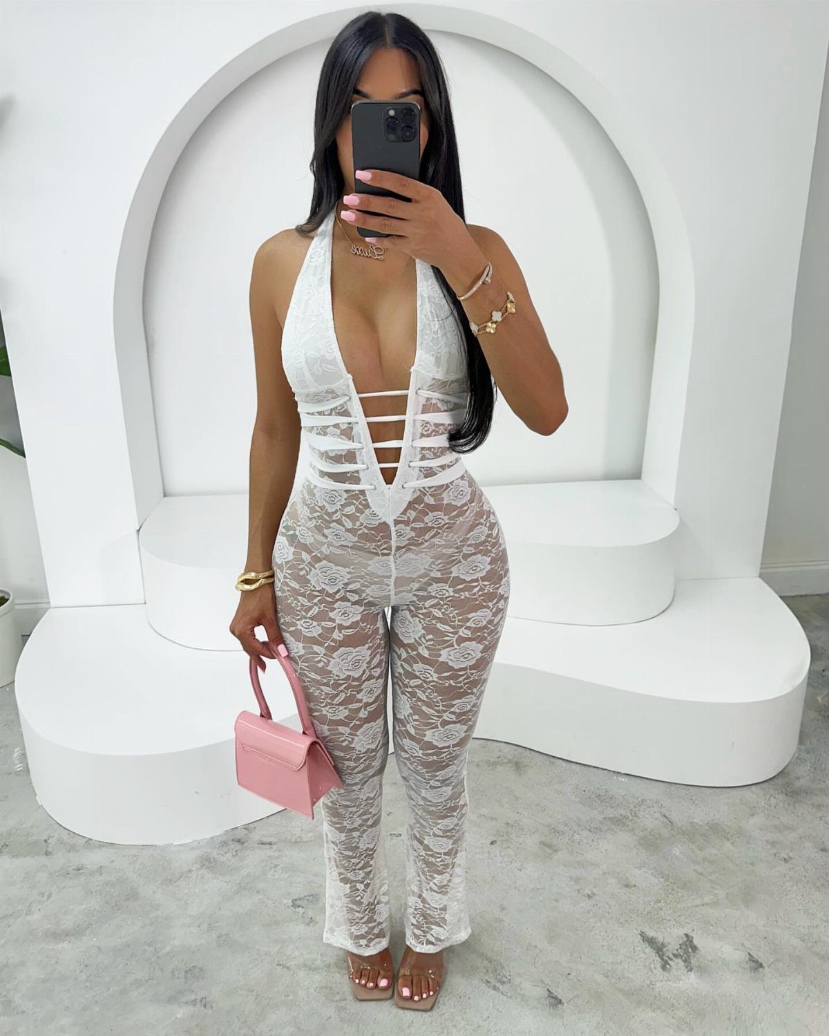 Outfit Ideas for Cancun: 13 Looks for Every Occasion 10 Woman wearing a white lace sheer jumpsuit with a small pink handbag.