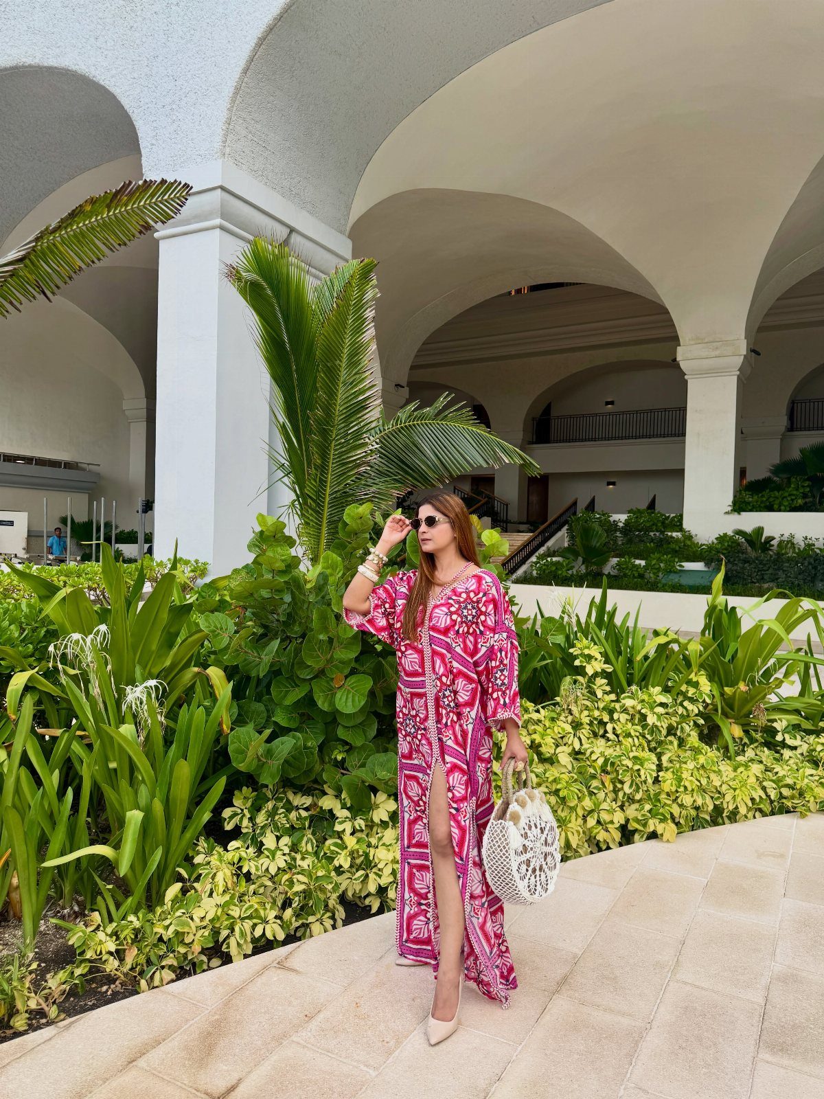 Outfit Ideas for Cancun: 13 Looks for Every Occasion 5 Woman in a pink and white printed maxi dress posing by tropical greenery.