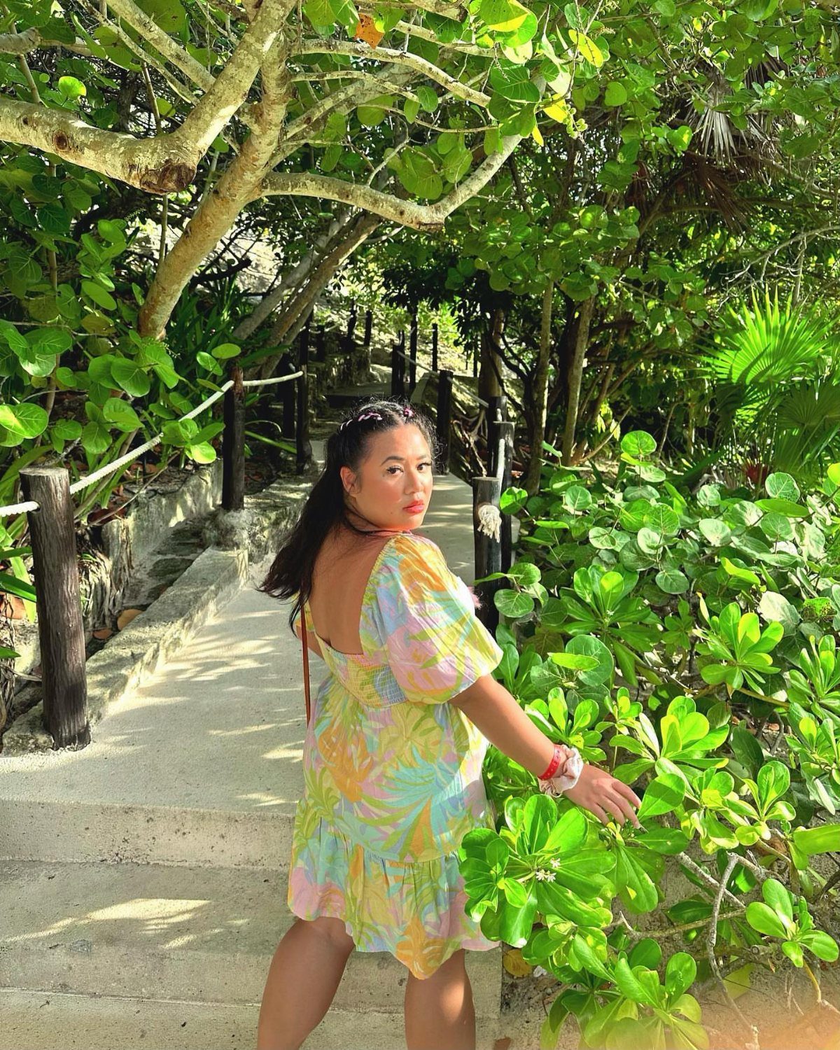 Outfit Ideas for Cancun: 13 Looks for Every Occasion 11 Woman in a colorful floral puff-sleeve sundress standing on a tropical garden path.