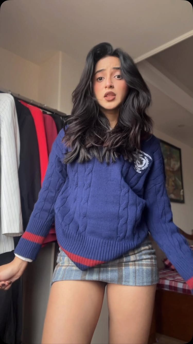 Woman wearing a blue cable knit sweater and a grey plaid mini skirt.