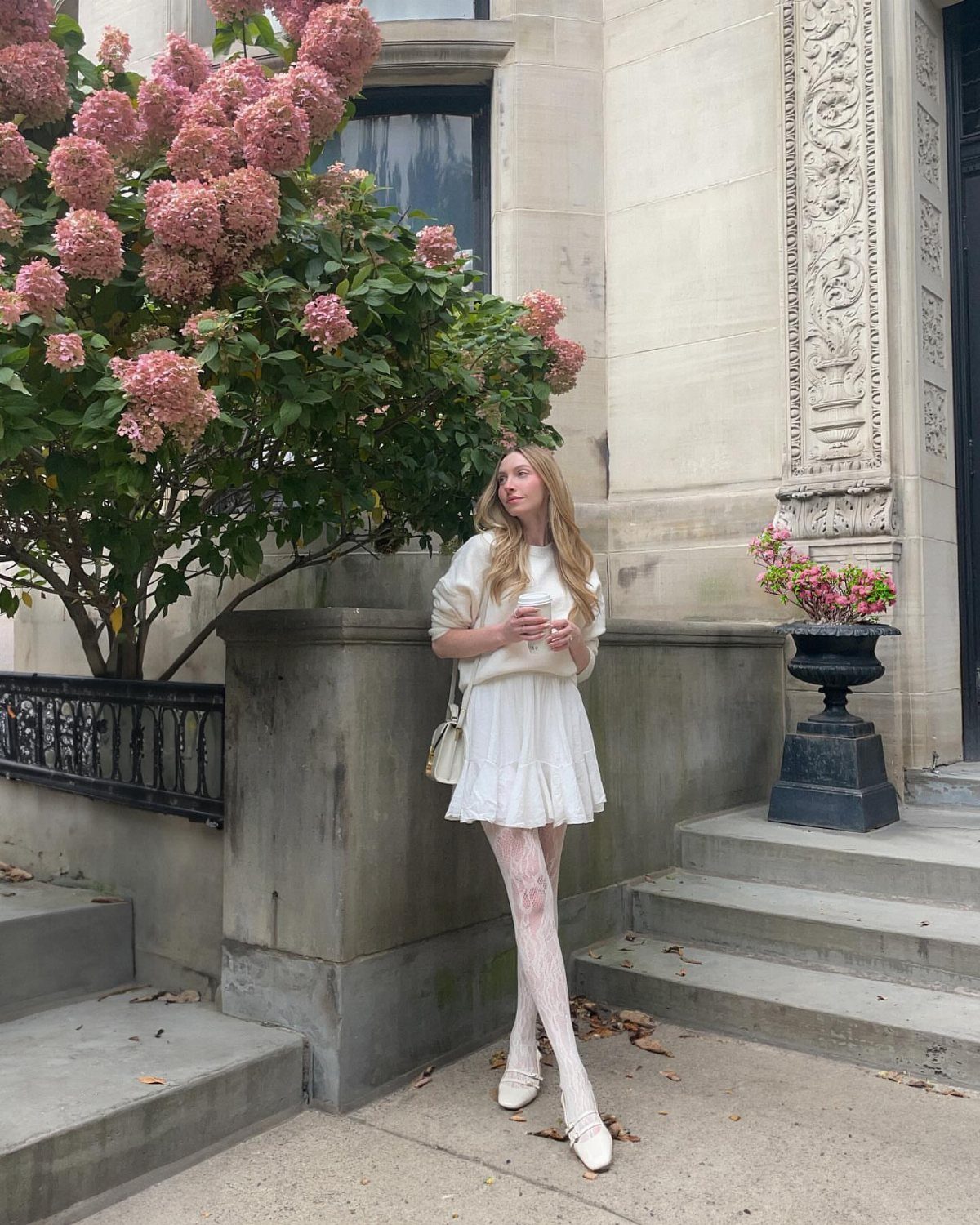 Woman in cream sweater, white pleated mini skirt, and white lace tights.