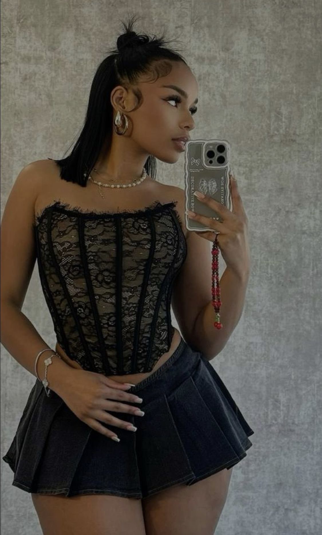 Woman wearing a black lace corset and dark denim pleated mini skirt.