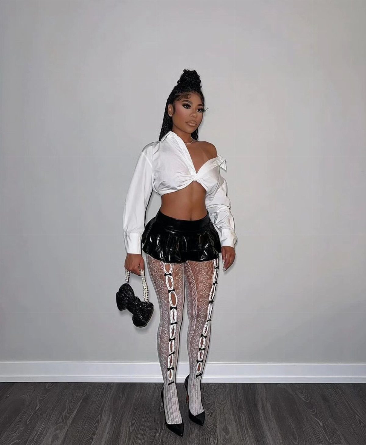 Woman wearing white wrap top, black leather pleated mini skirt, and lace tights.