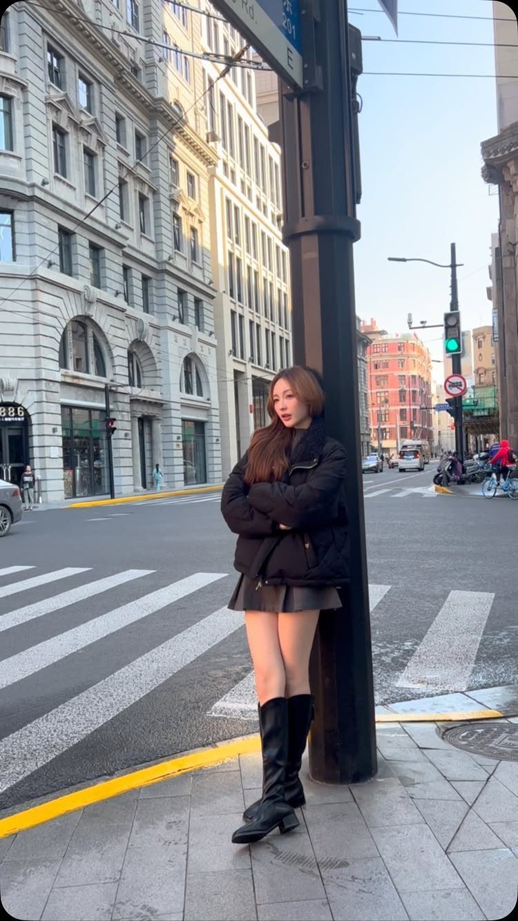 Woman in black puffer jacket and mini skirt standing on a city street.