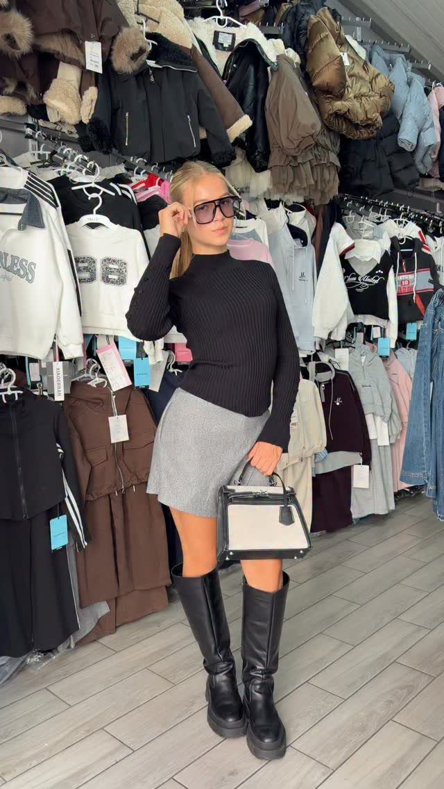 Woman in black turtleneck and grey mini skirt wearing tall black leather boots.