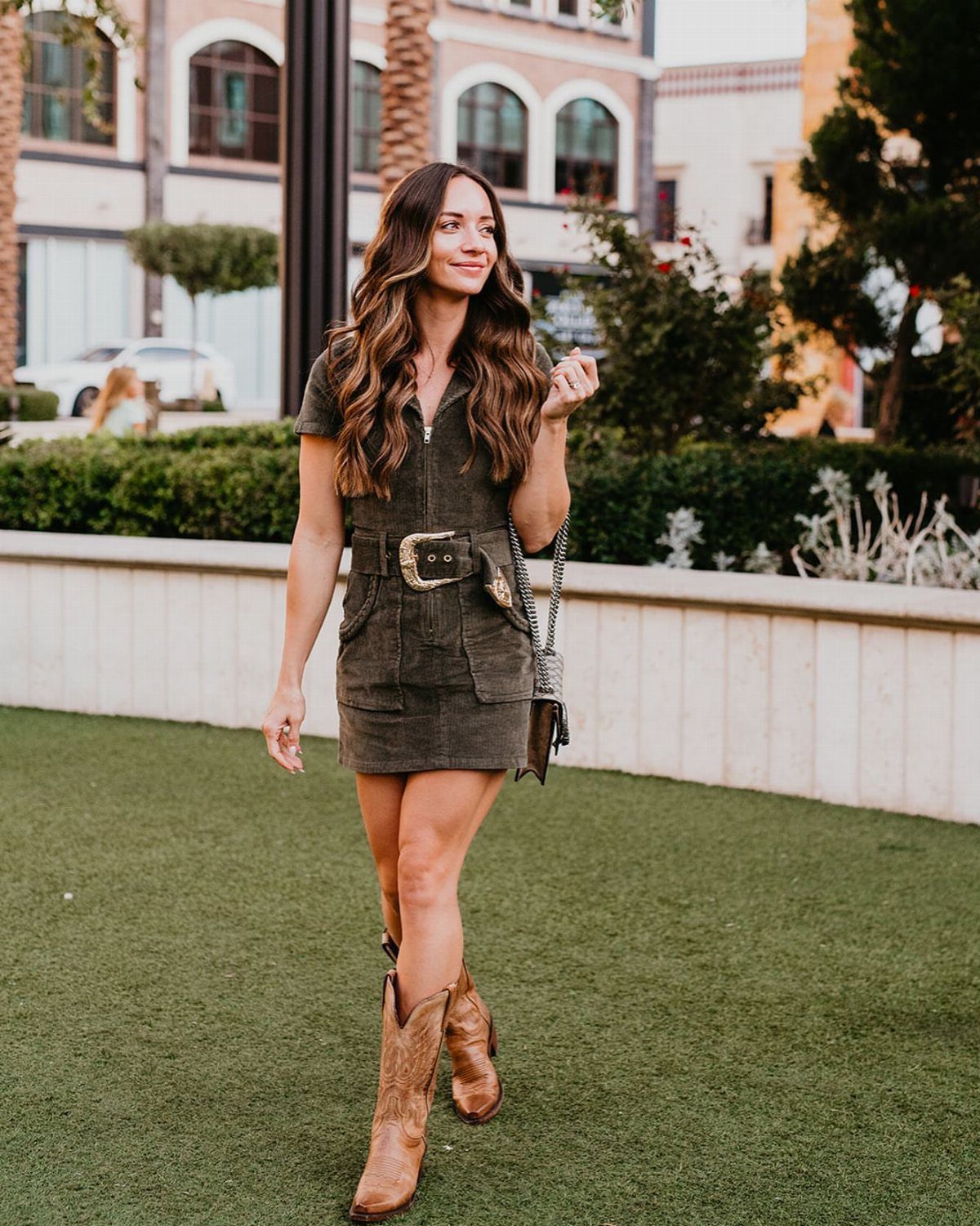 Outfit with Cowboy Boots: 6 Ways From Casual to Dressy 5 Woman in olive green utility dress and brown leather cowboy boots on green grass.
