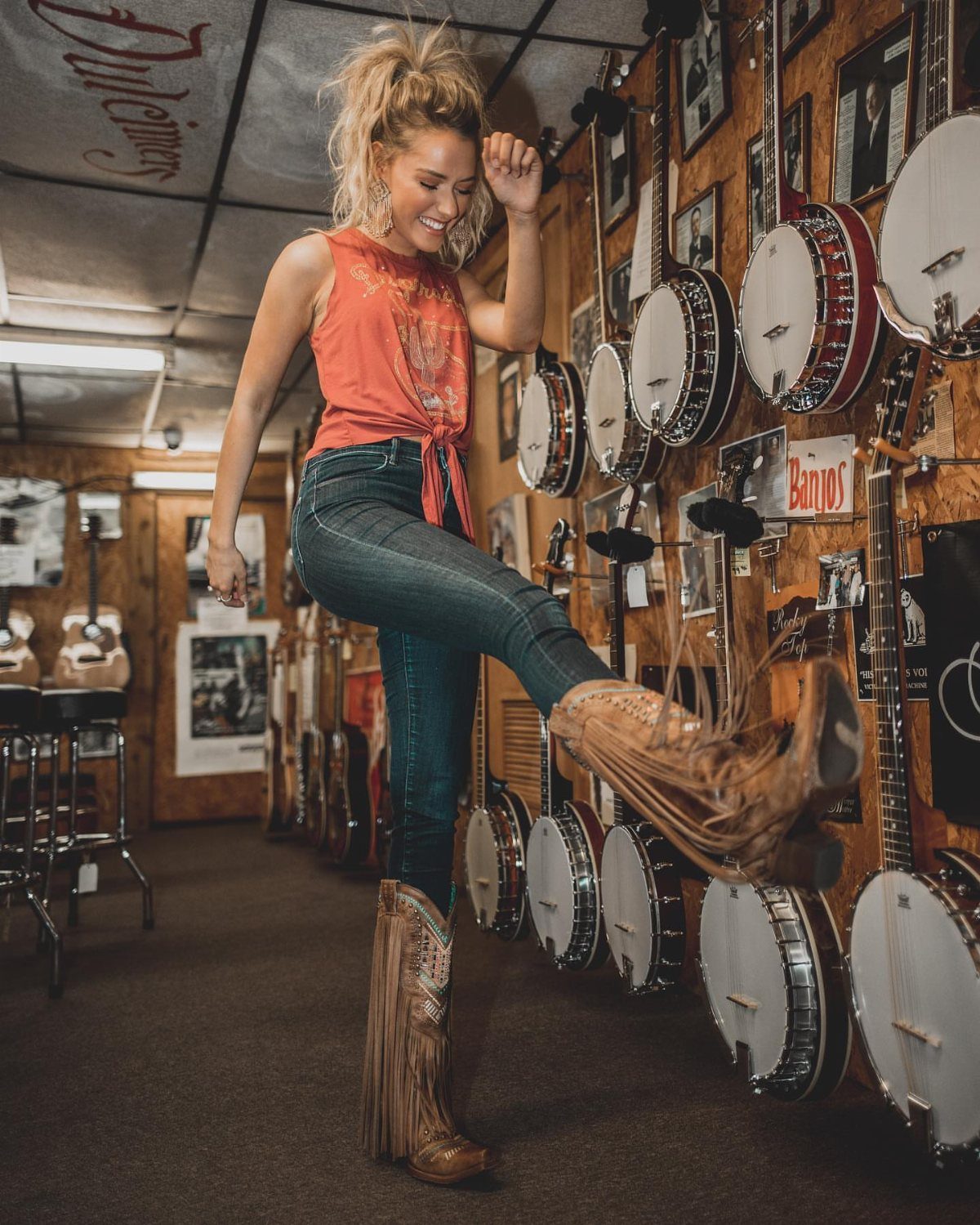 Outfit with Cowboy Boots: 6 Ways From Casual to Dressy 1 Woman in orange top and blue jeans wearing brown fringed cowboy boots.