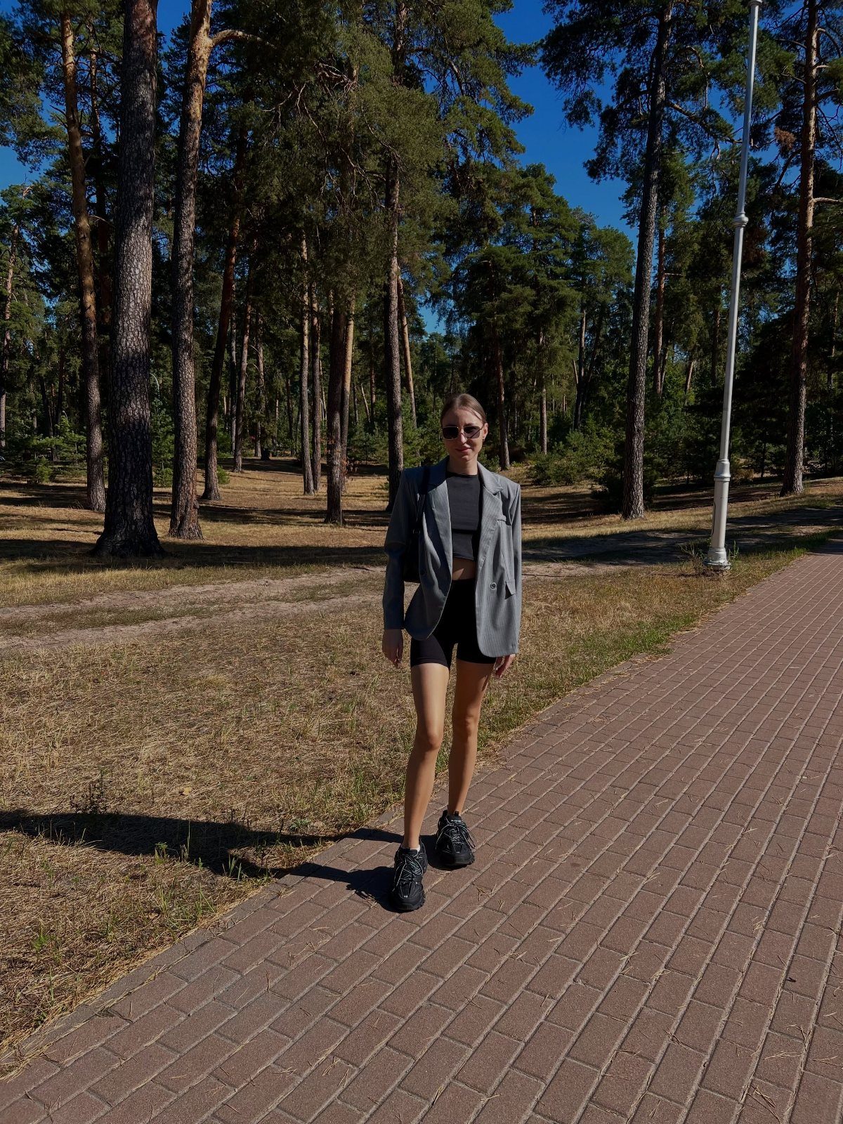 11 Outfits for Teens: Street to Semiformal Style Ideas 3 Young woman wearing a grey oversized blazer, black biker shorts, and chunky sneakers in a forest.