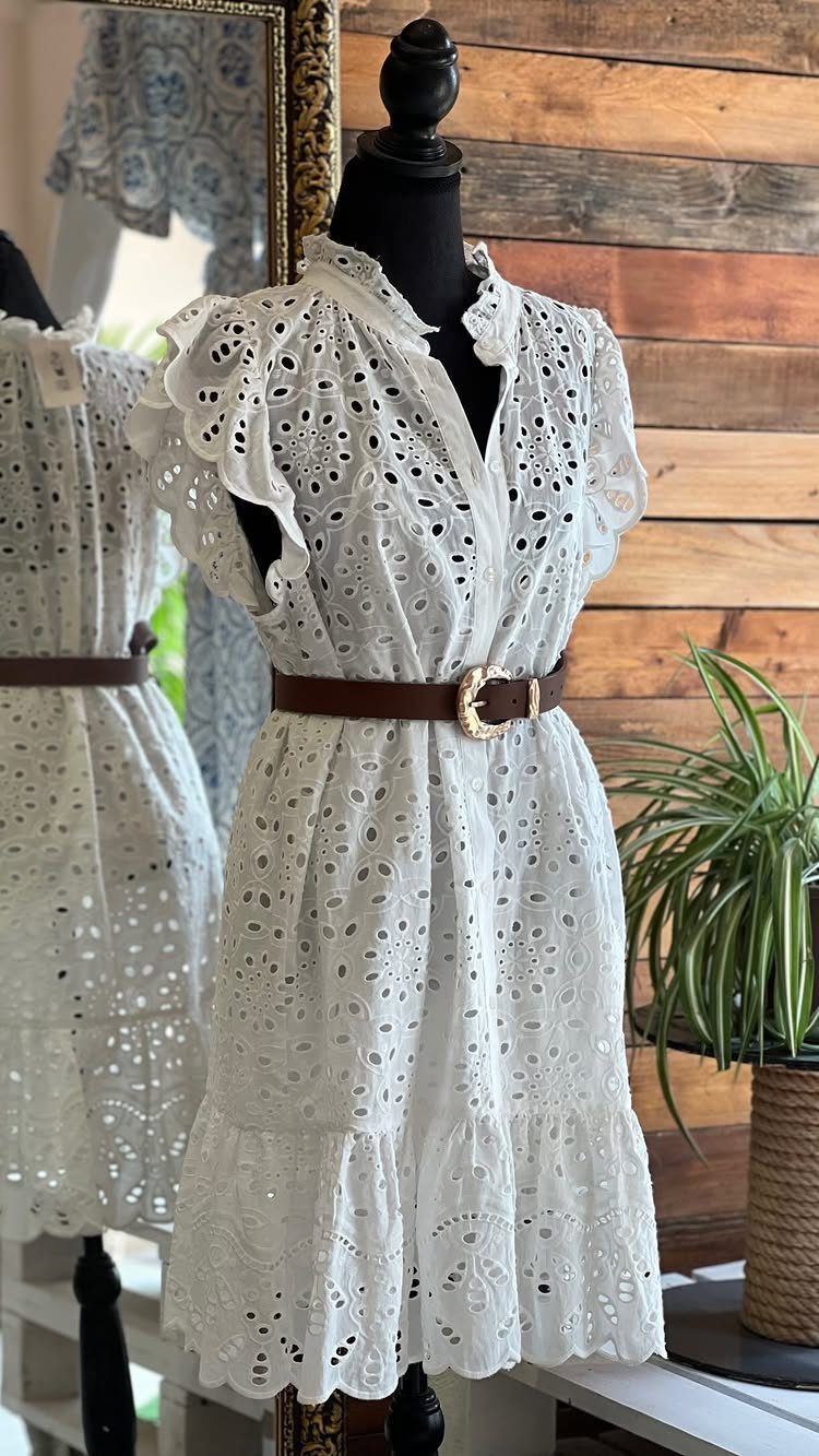 White eyelet design dress with ruffled sleeves and a brown belt on a mannequin.