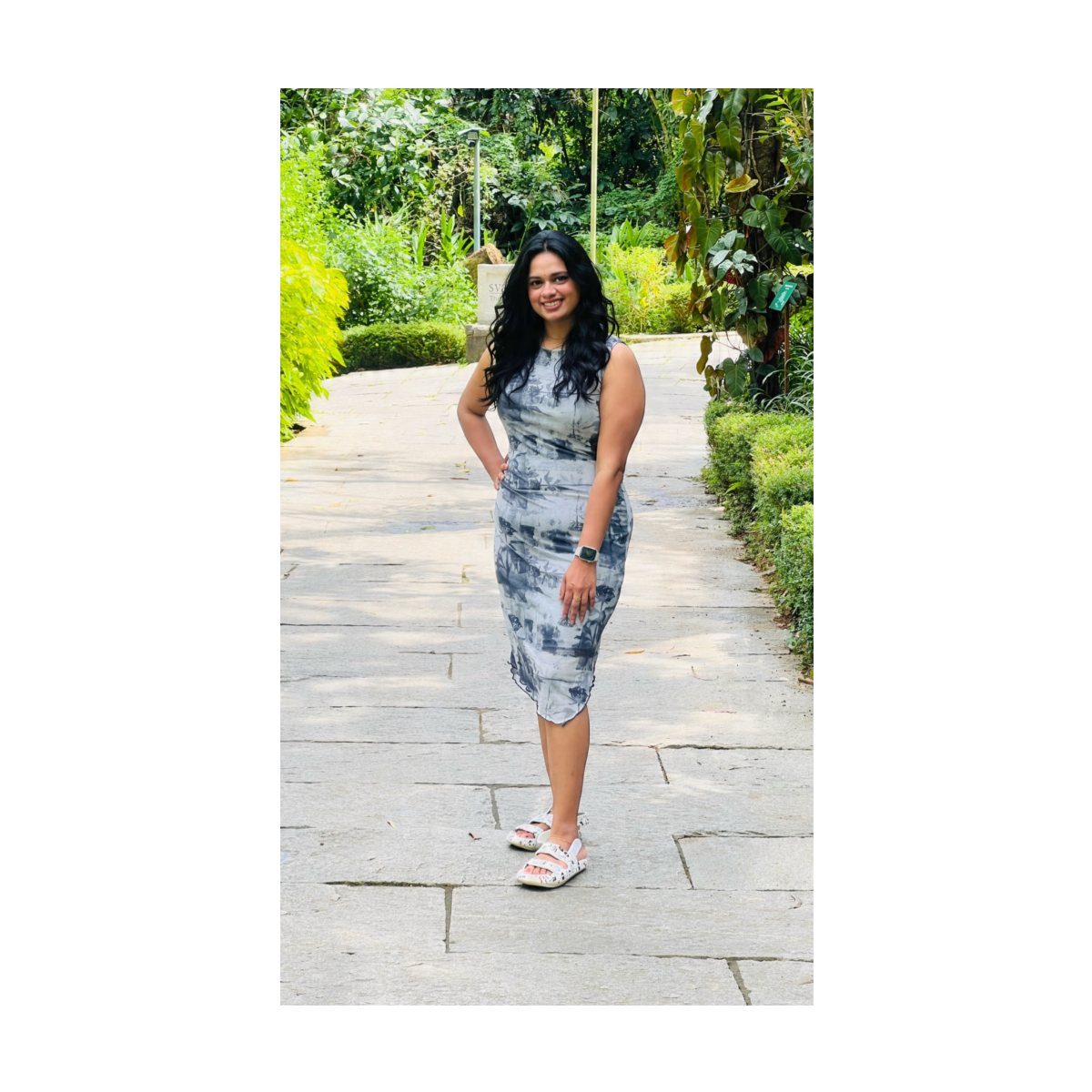 Woman in a sleeveless tie-dye midi dress standing on a stone garden path.