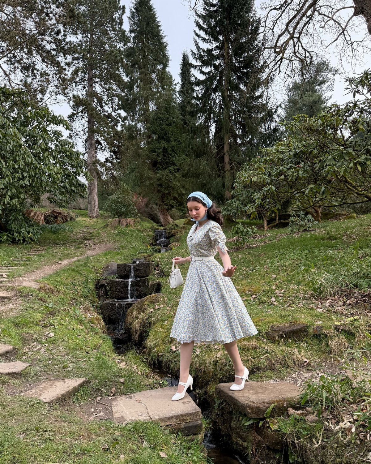 Woman in a vintage-style floral midi dress posing in a green forest garden.