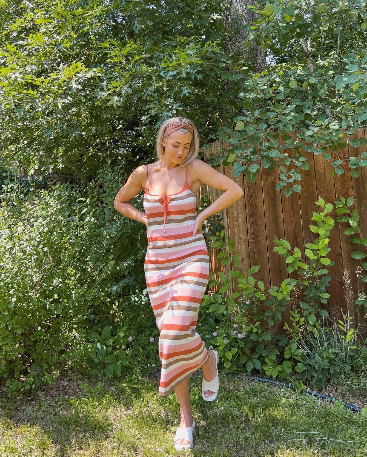 Woman posing in a striped orange and white wrap-style midi dress in a garden.