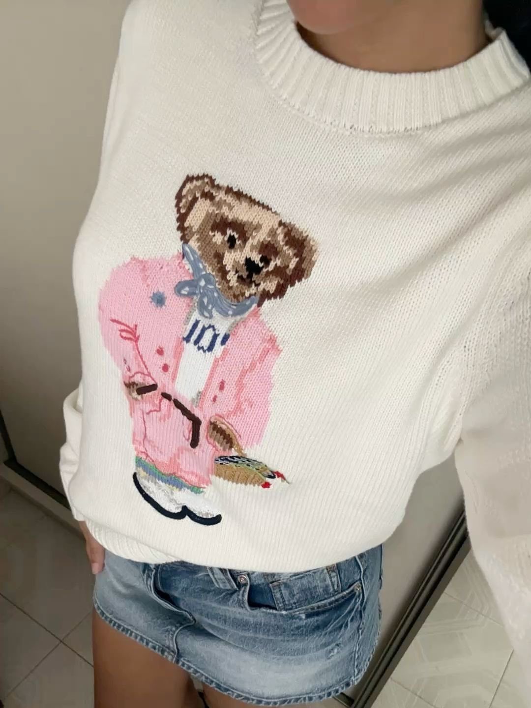 White bear sweater with a pink blazer graphic and a denim mini skirt.