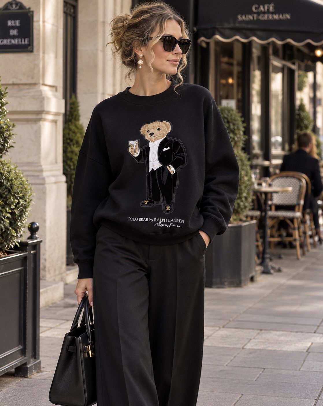 Woman wearing a black Polo bear sweatshirt and black trousers on a city street.