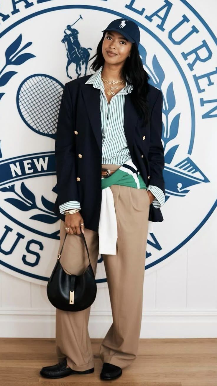 Woman in navy blazer and tan trousers posing before a Ralph Lauren logo.