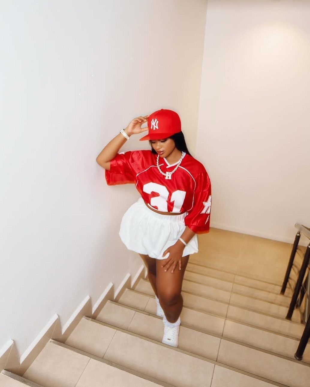 15 Preppy Summer Outfits to Wear All Season Long 3 Woman in red football jersey and white bubble skirt posing on stairs.