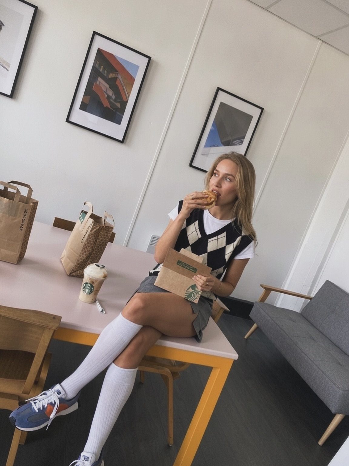 15 Preppy Summer Outfits to Wear All Season Long 10 Woman in a diamond sweater vest and pleated skirt eating a burger.