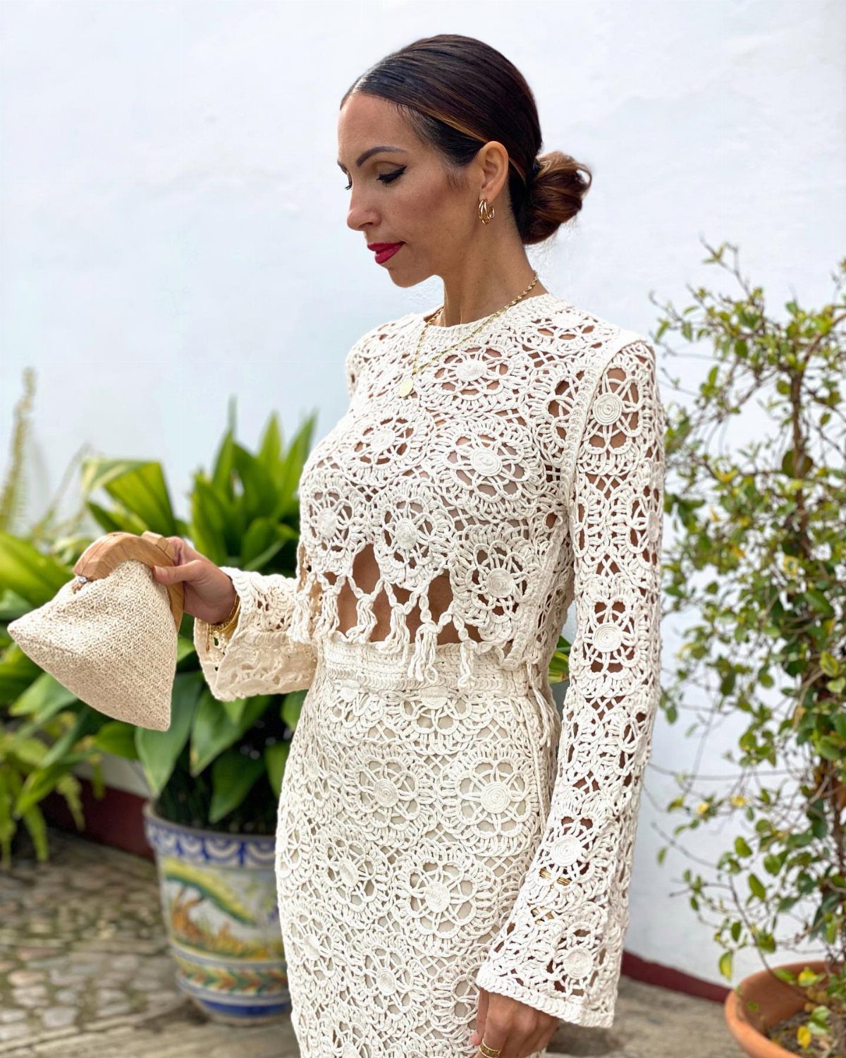 Woman in a cream crochet cropped top and midi skirt holding a straw bag.