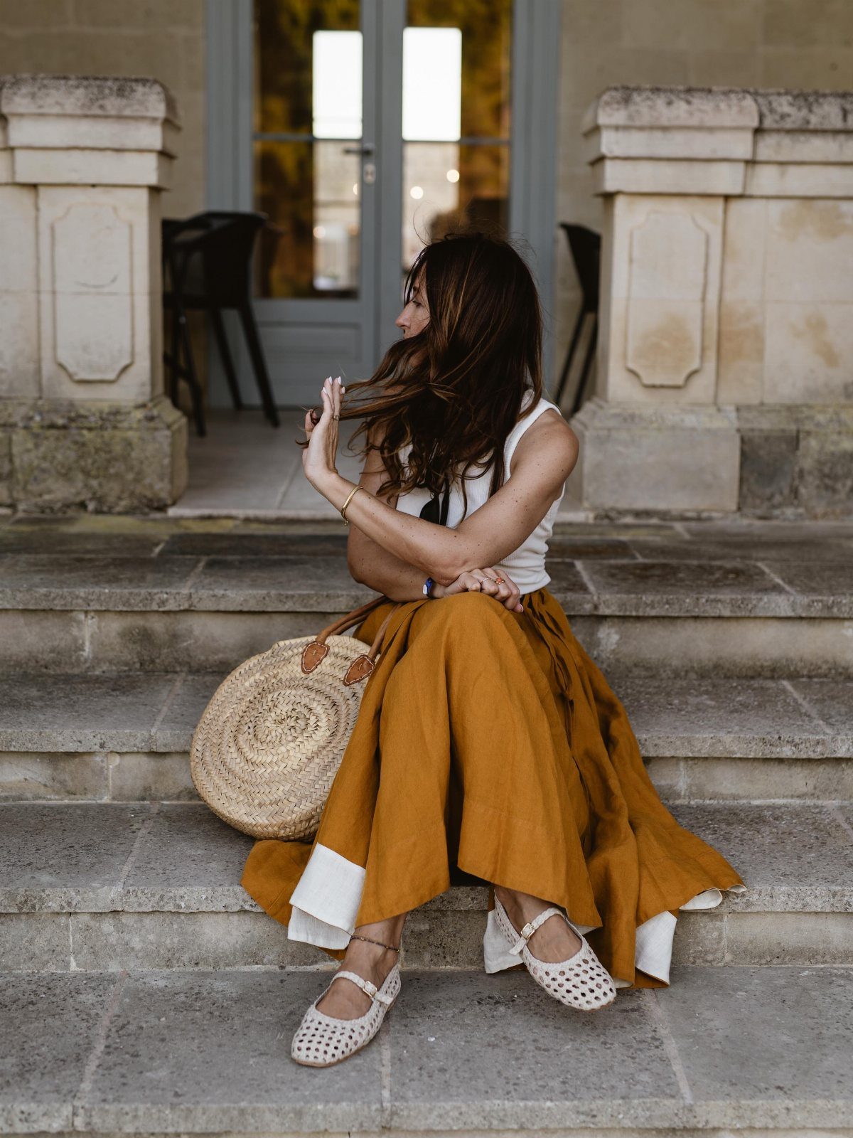 Woman in mustard yellow skirt and white top sitting on stone steps.