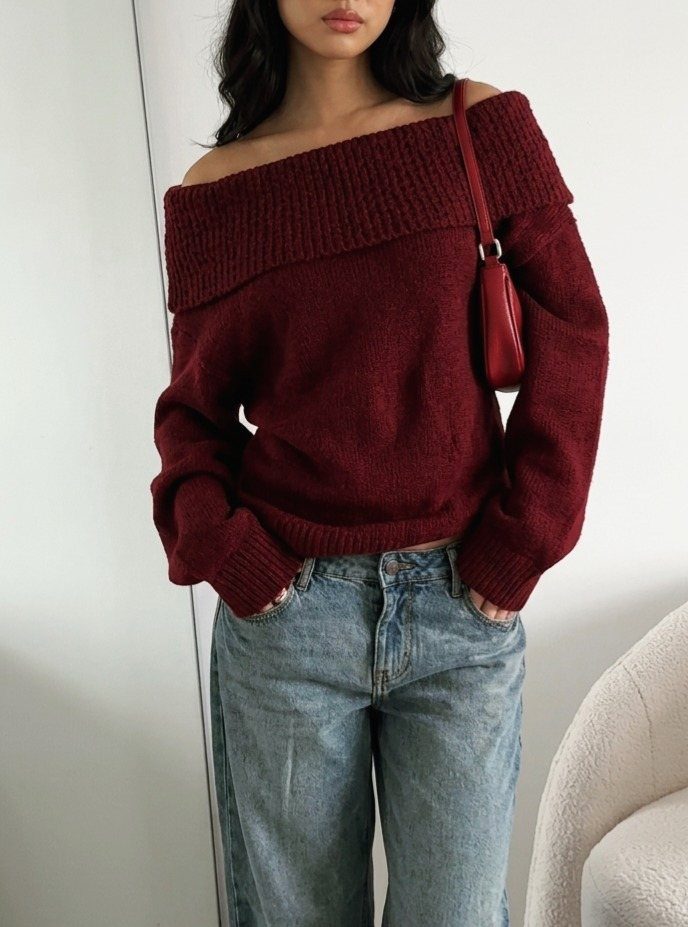 Woman wearing a maroon off-the-shoulder knit sweater and light-wash blue denim jeans.