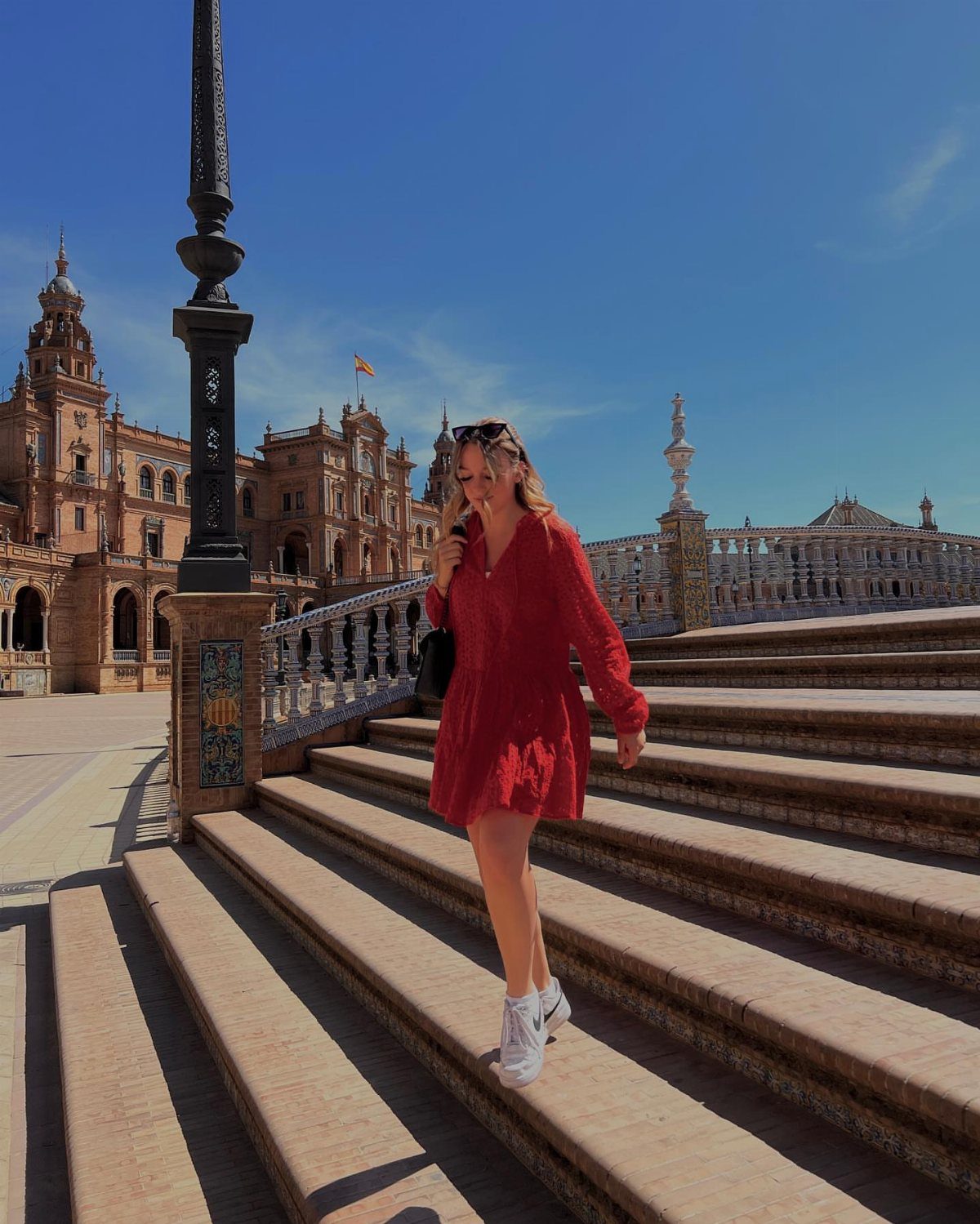 Woman in a red mini dress and white sneakers walking down stone stairs.