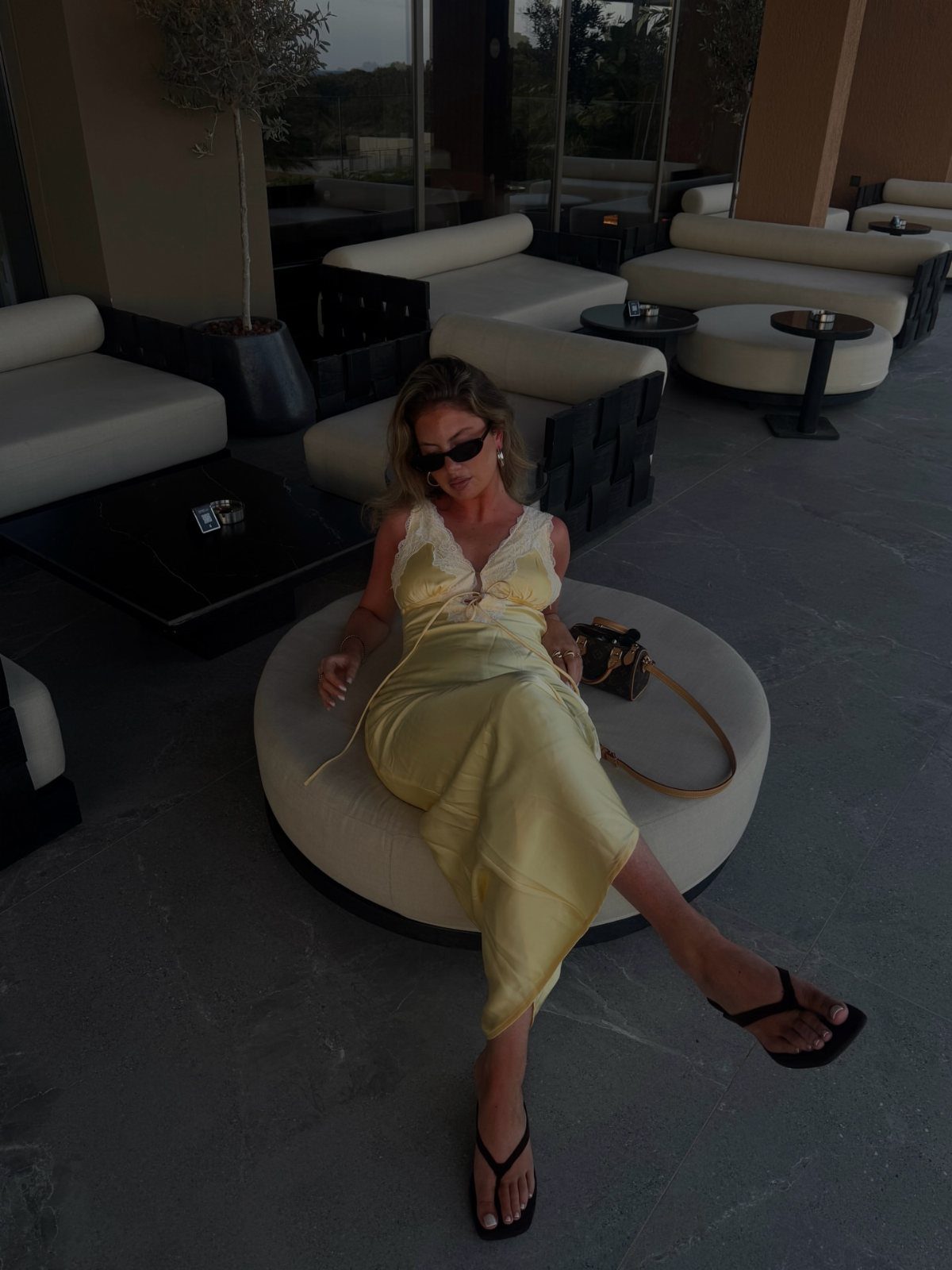Woman in a yellow satin maxi dress with lace bodice sitting in a lounge.