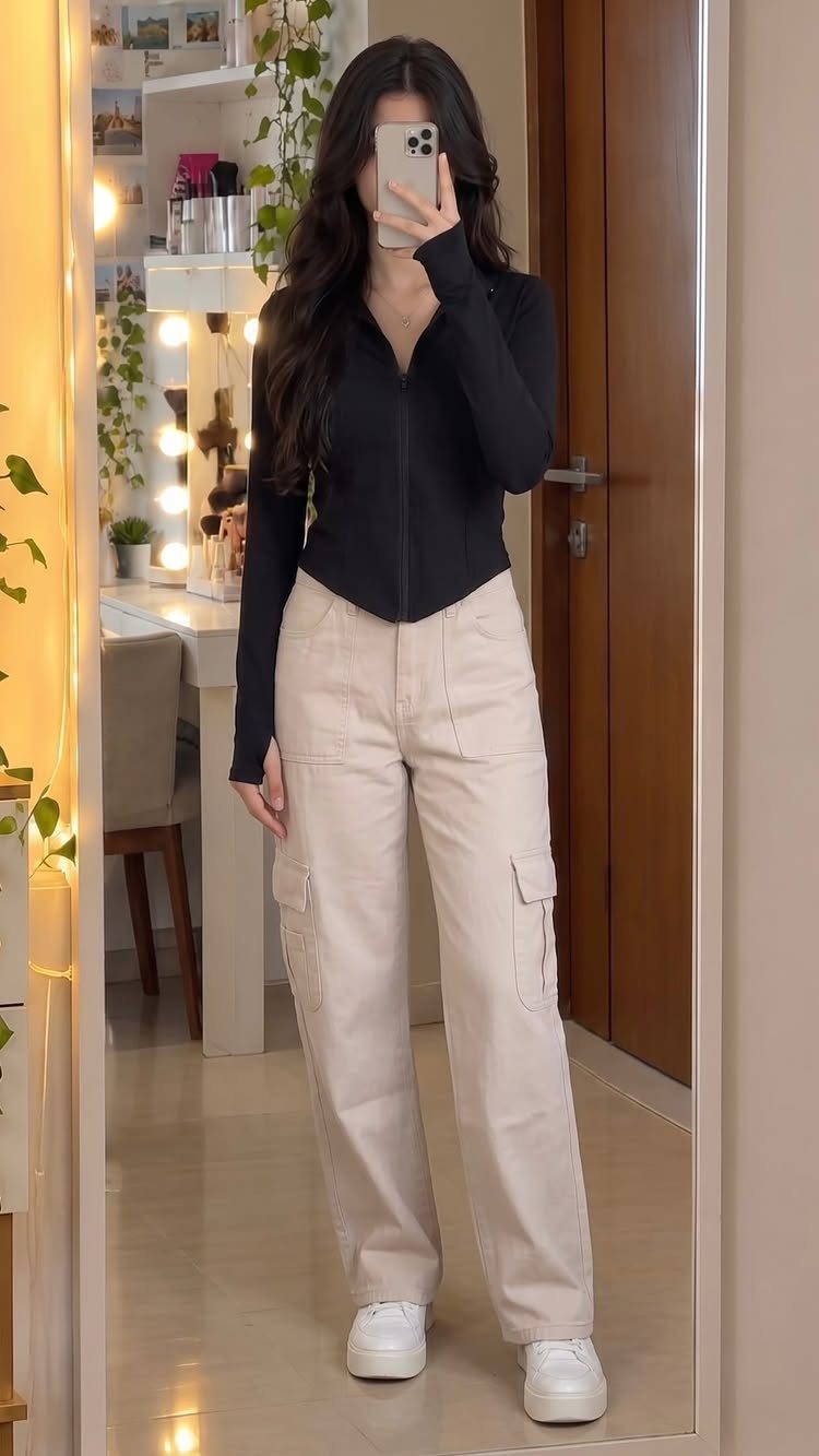 12 Sporty Chic Outfits That Work Beyond the Gym 4 Woman wearing beige cargo pants, black zip-up top, and white sneakers in mirror selfie.
