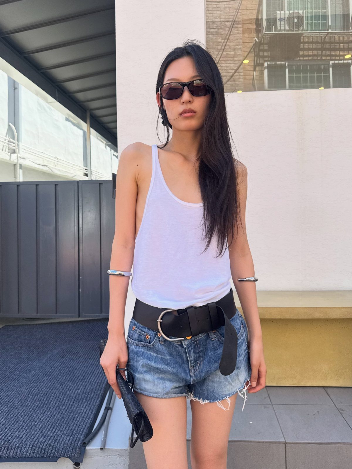 12 Sporty Chic Outfits That Work Beyond the Gym 12 Woman wearing a white tank top, denim shorts, and black belt in a sporty chic style.