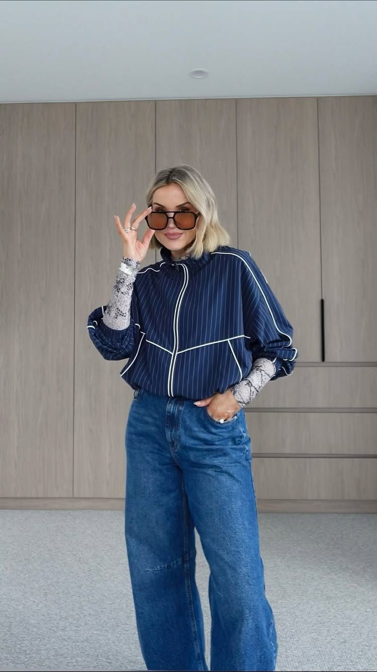 12 Sporty Chic Outfits That Work Beyond the Gym 6 Woman in oversized pinstriped shirt and wide-leg blue jeans posing indoors.