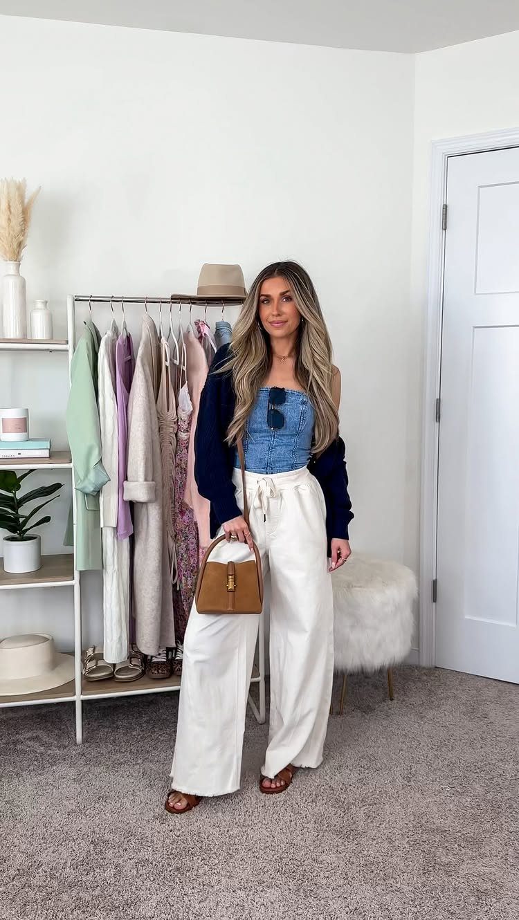 A woman posing in a denim top, navy cardigan, and white wide-leg trousers.
