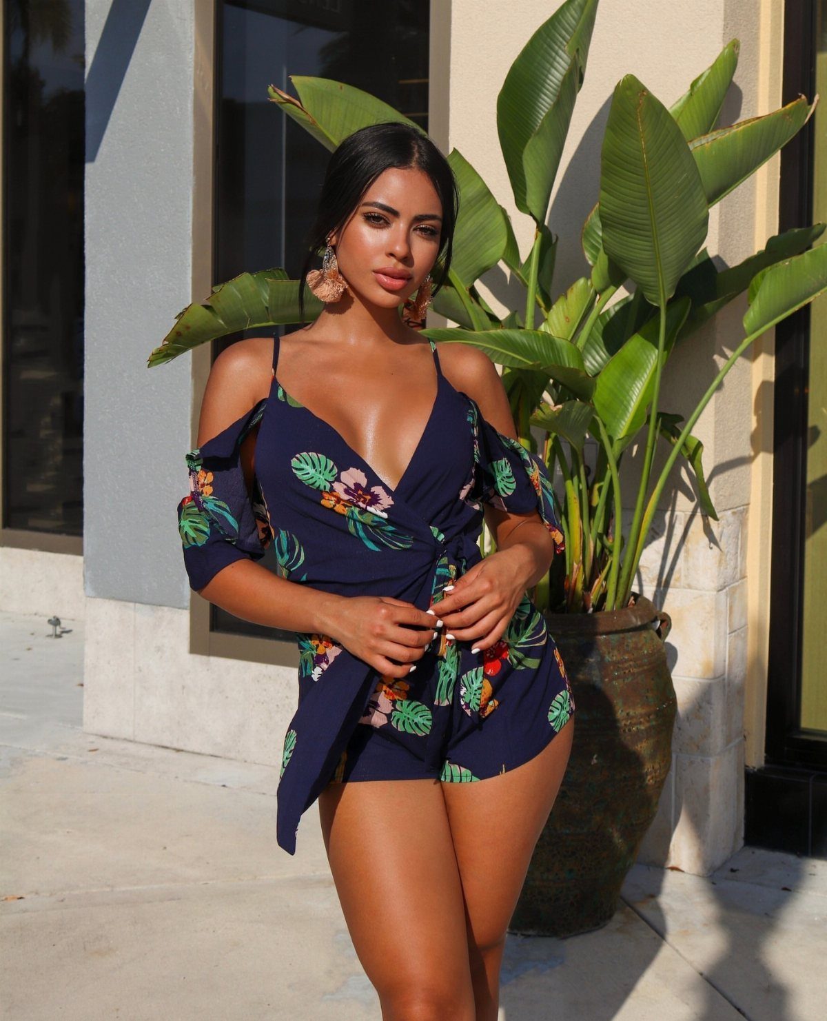 Woman in a navy tropical print romper standing in front of large green leaves.