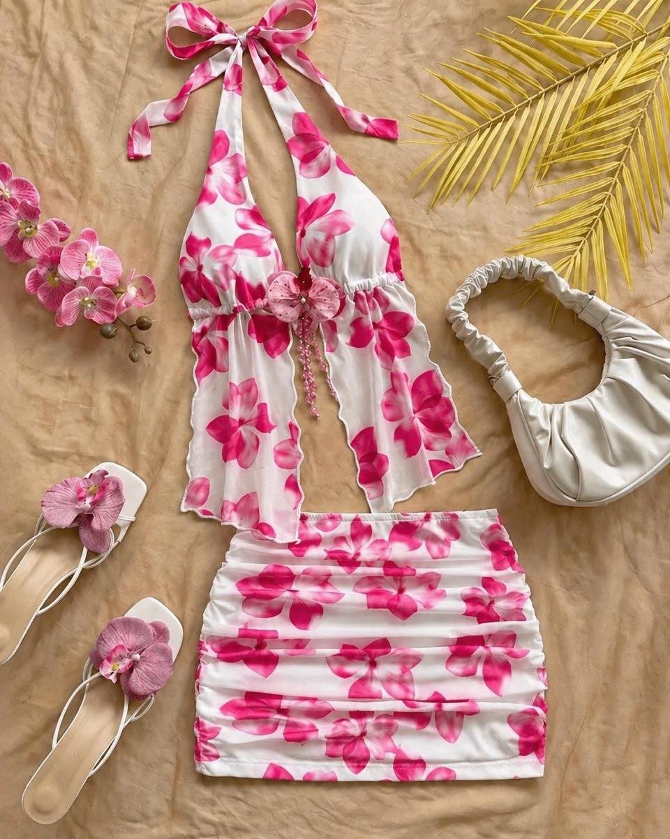 Pink floral two-piece set with a halter top and ruched skirt laid on tan fabric.