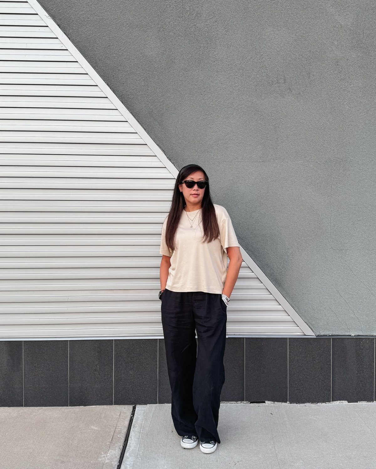 11 Spring Summer Outfits You'll Reach for All Season Long 2 Woman wearing a drapey cream t-shirt and wide-leg black pants with white sneakers.