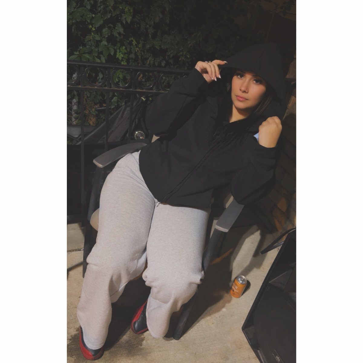 Woman wearing a black zip-up hoodie and grey joggers sitting outdoors at night.