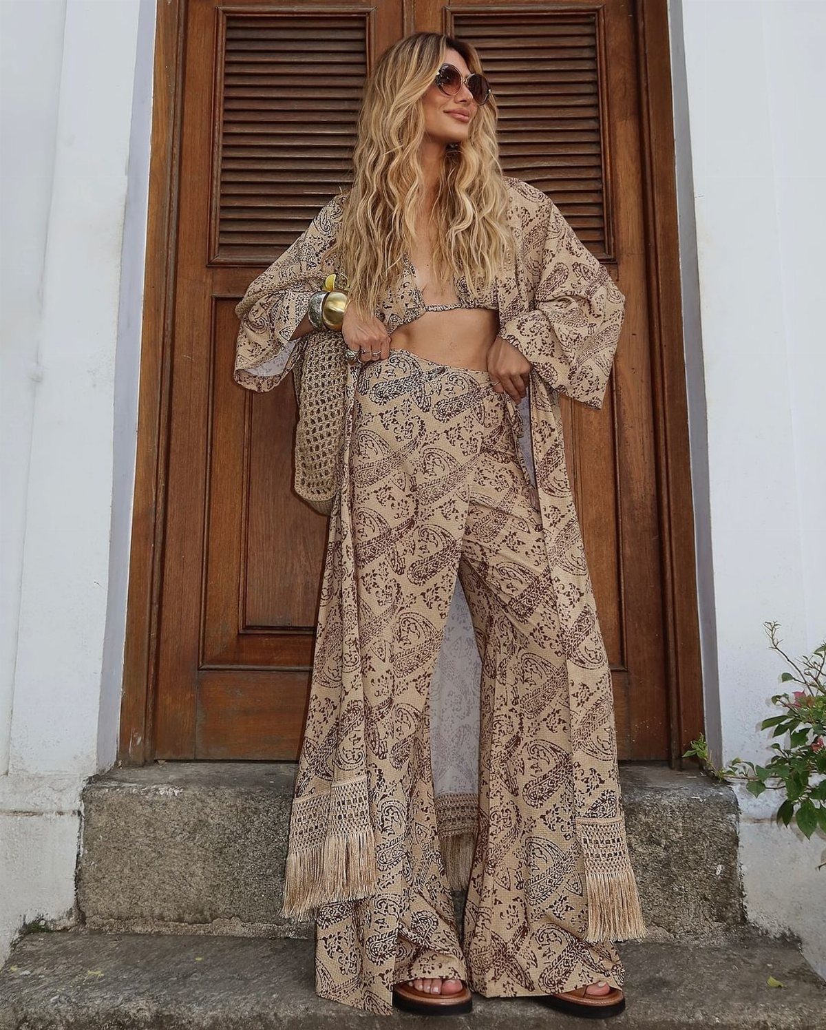 Woman wearing a patterned beige lightweight kimono with matching wide-leg trousers and bralette.