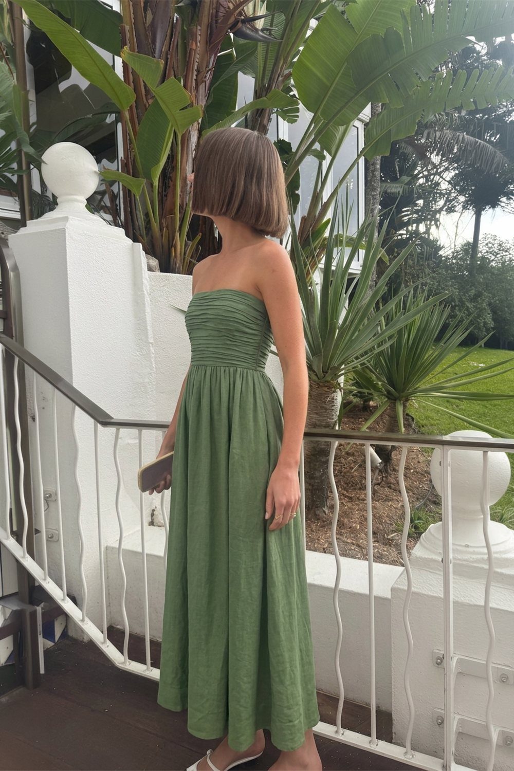 Woman wearing a strapless olive green linen maxi dress on a tropical balcony.