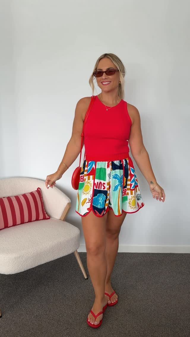 Woman wearing a red tank top and colorful patterned mini skirt with red sandals.