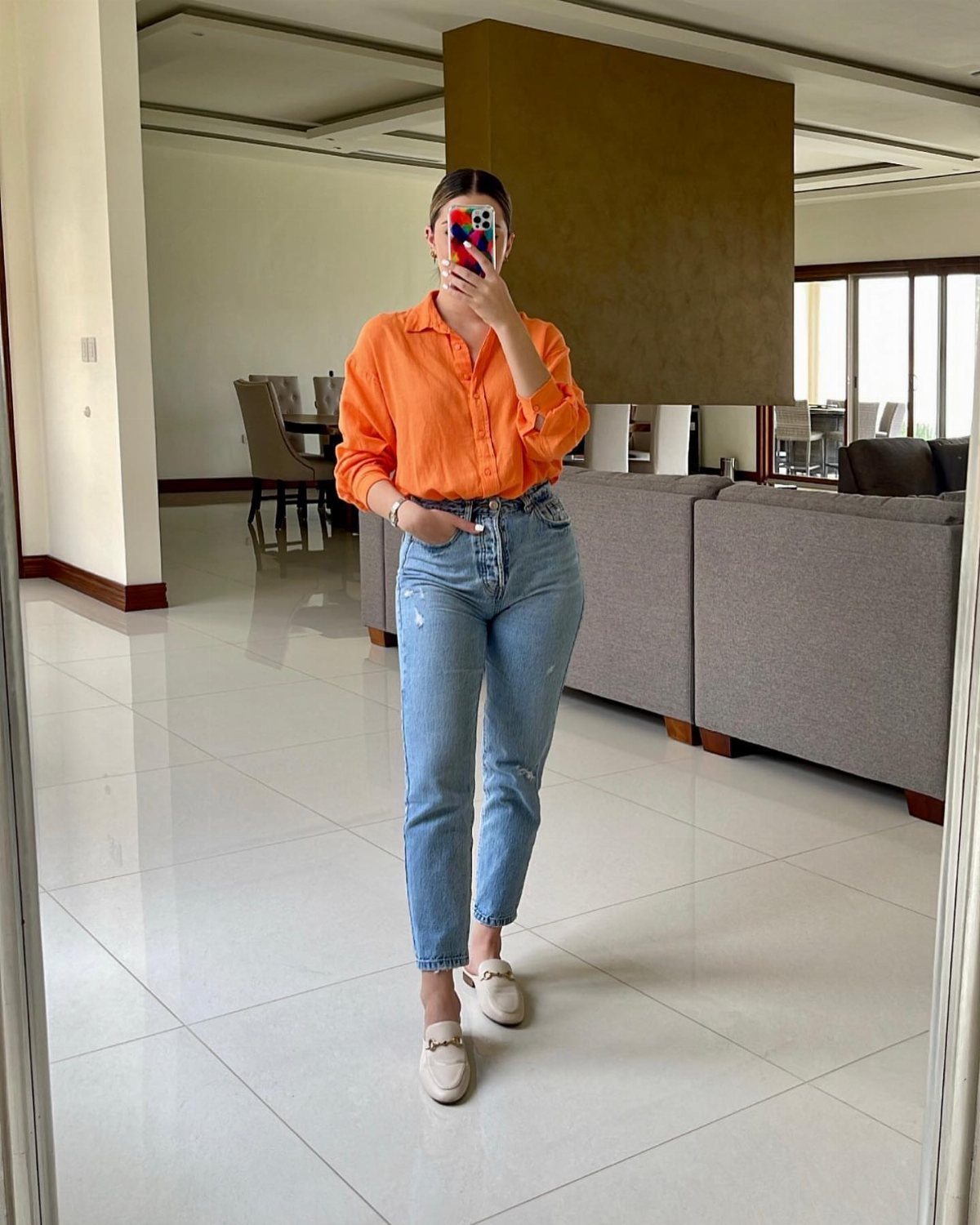 Woman wearing an orange puff-sleeve blouse and high-waisted blue mom jeans.