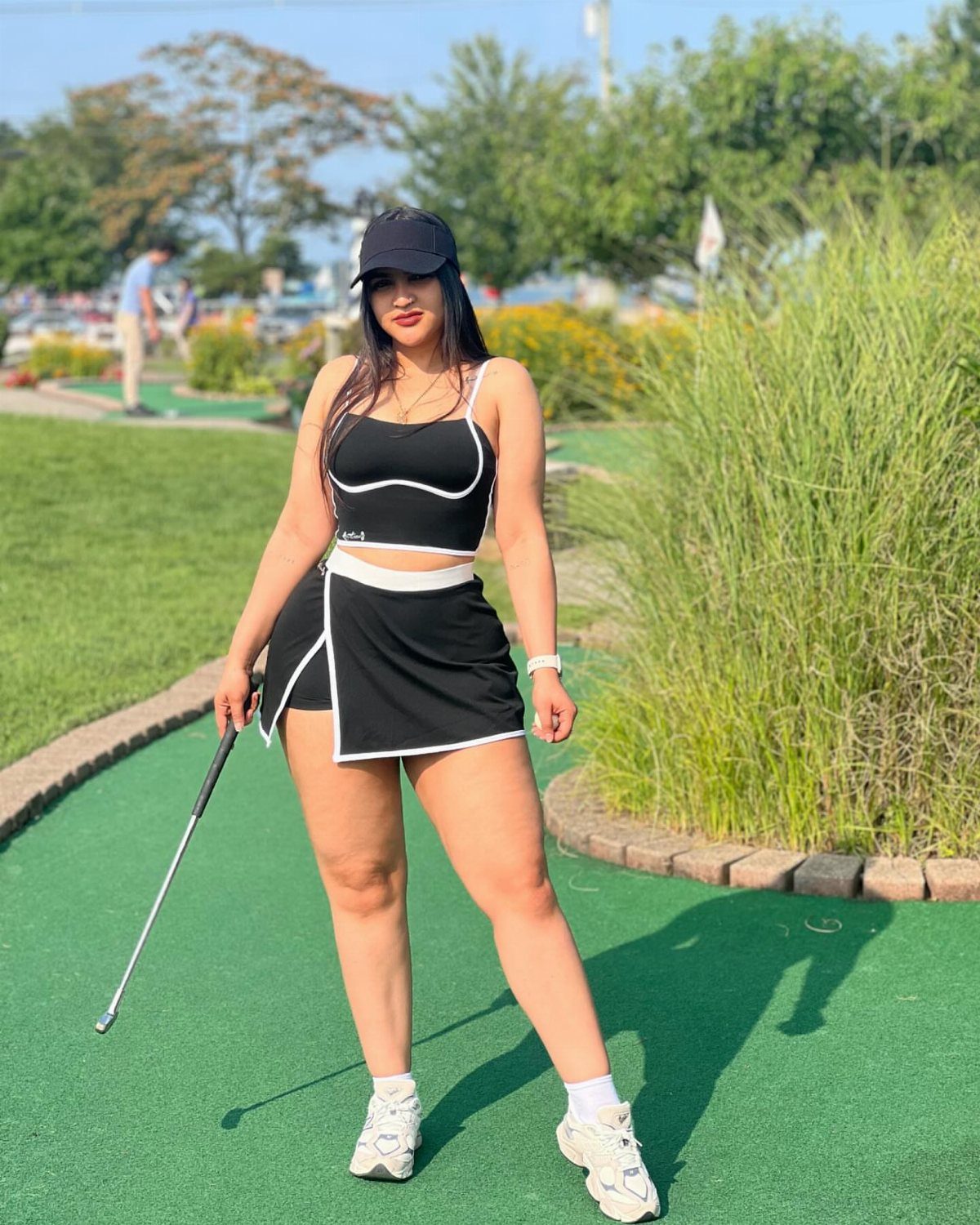 Woman in black tank top and skort holding a golf club on a green.