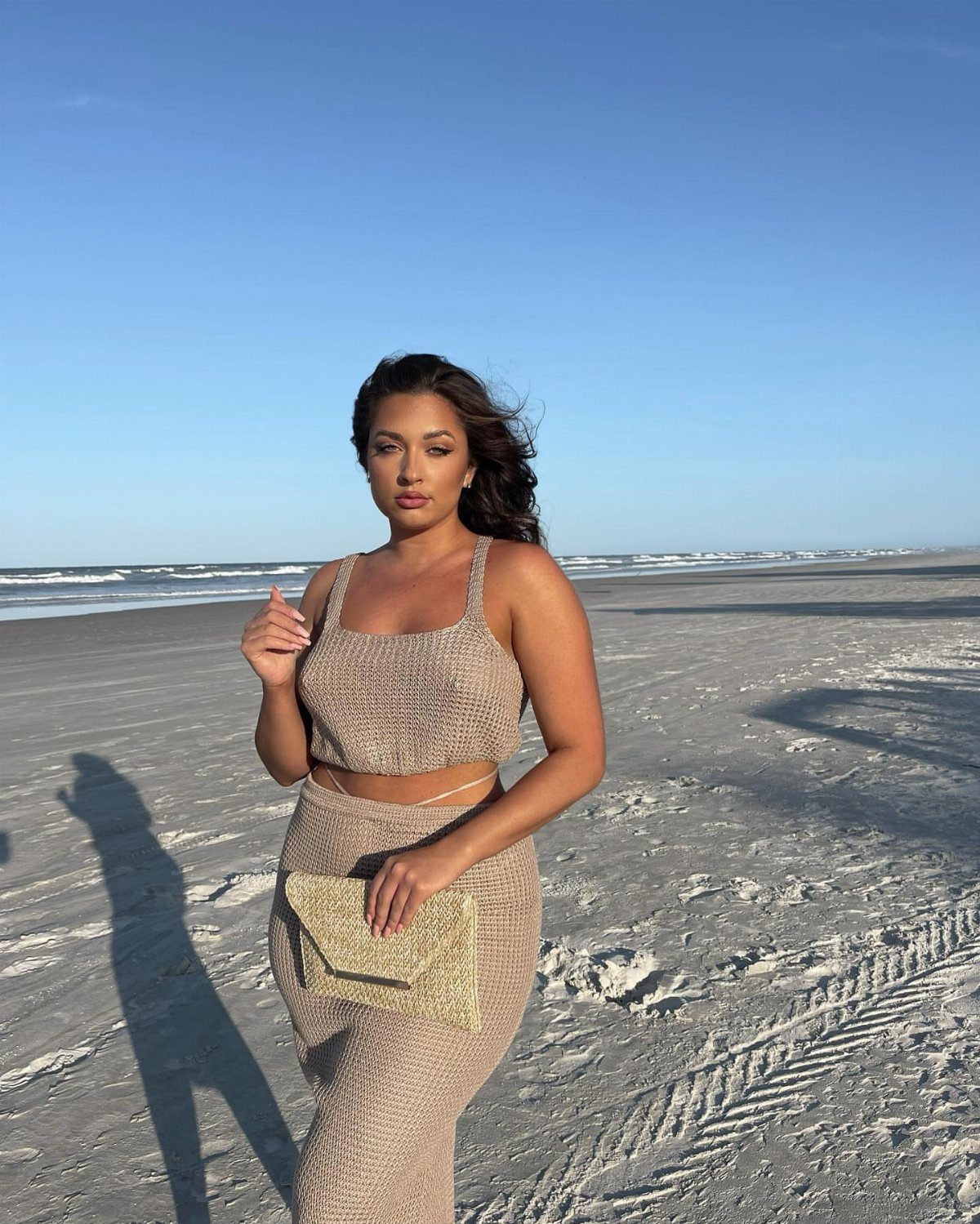 Woman in a beige crochet two-piece set posing on a sandy beach.