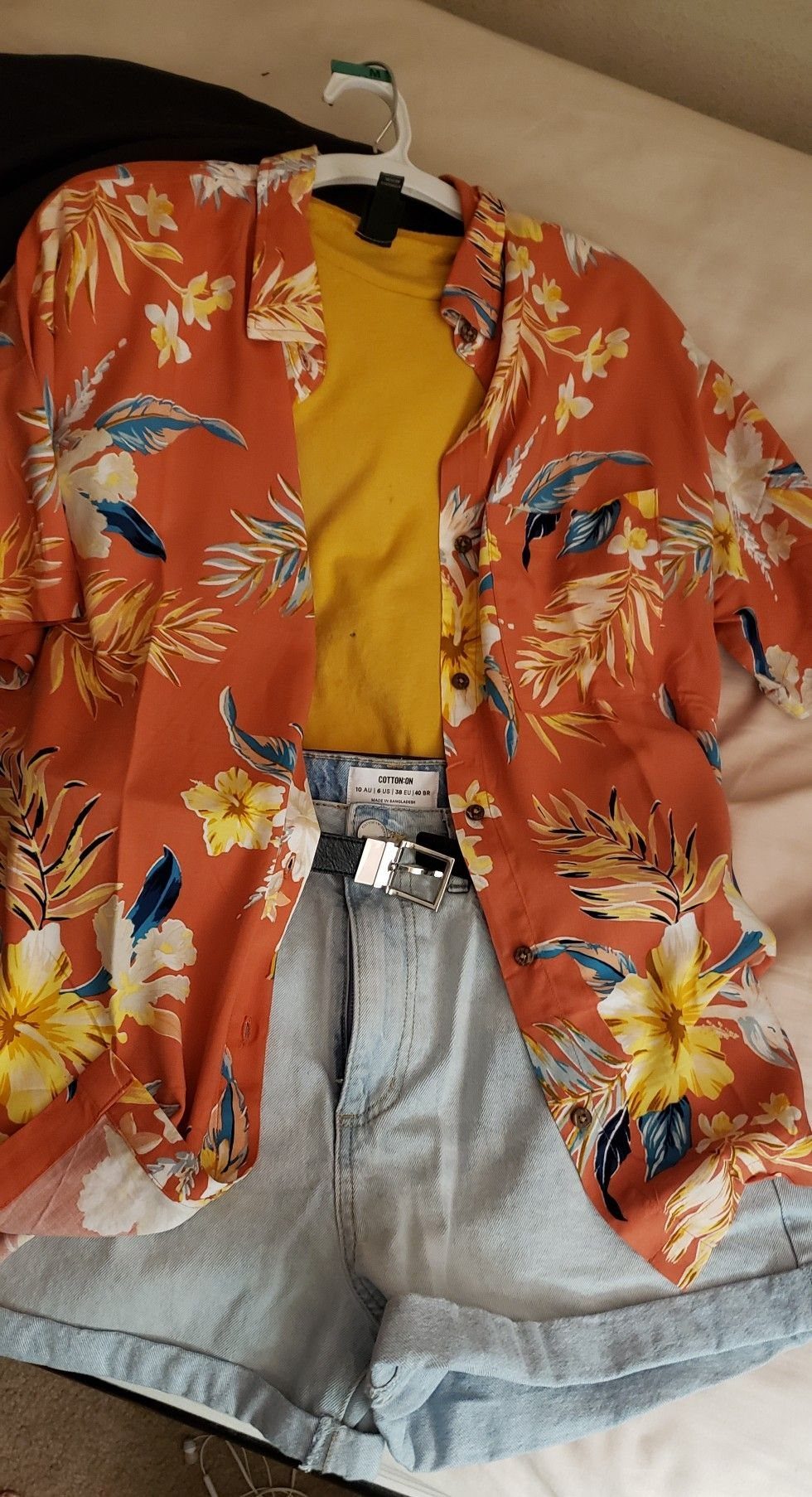 An orange tropical print shirt layered over a yellow tank top and light blue denim shorts.