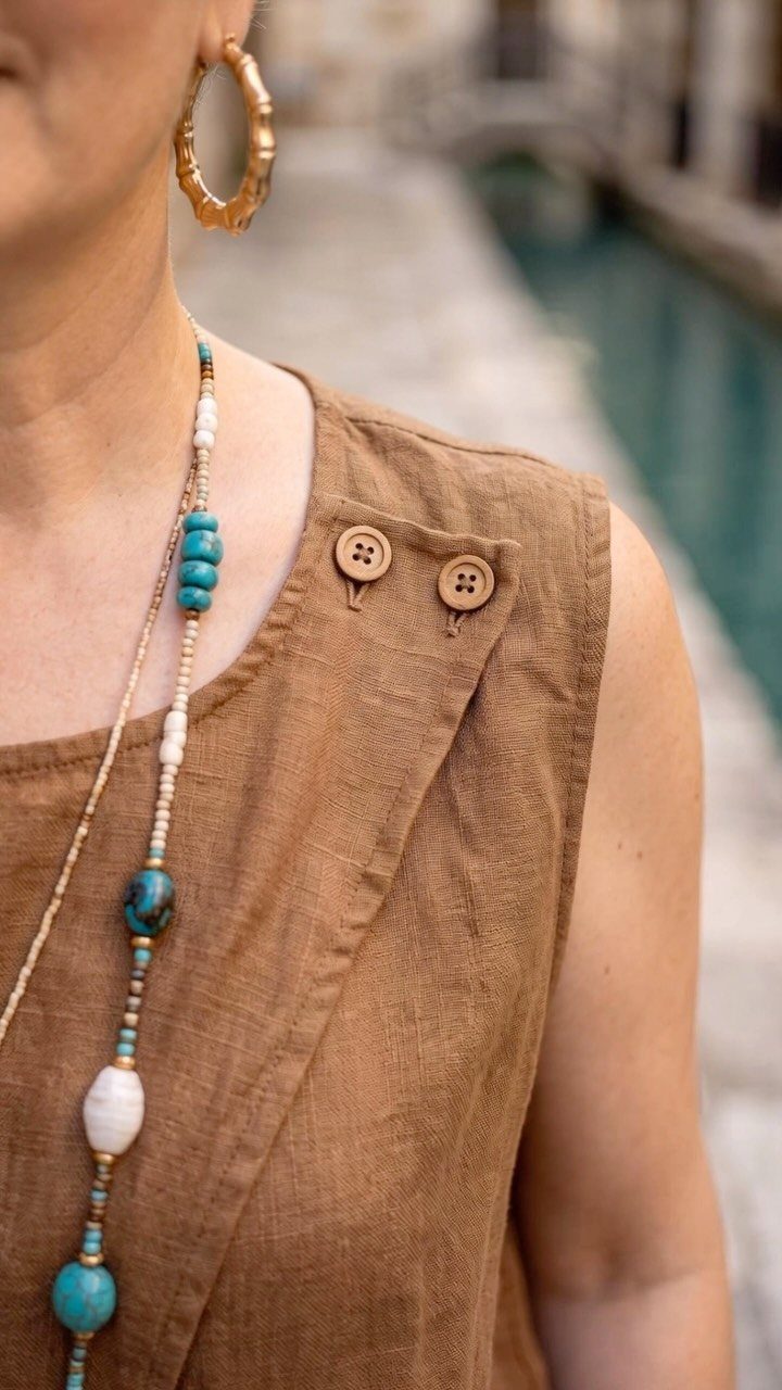 Woman wearing a brown linen sleeveless top and turquoise beaded necklace outdoors.